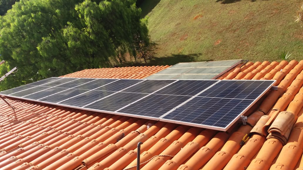 Fileira de painéis solares em telhado de telha laranja com área verde abaixo